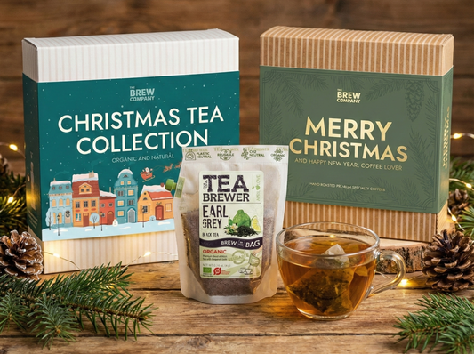 Kaffee Geschenkset Weihnachten mit Merry Christmas Box, Christmas Tea Collection und Earl Grey Tea Brewer Beutel neben Tasse schwarzem Tee auf rustikalem Holztisch, festliche Dekoration.
